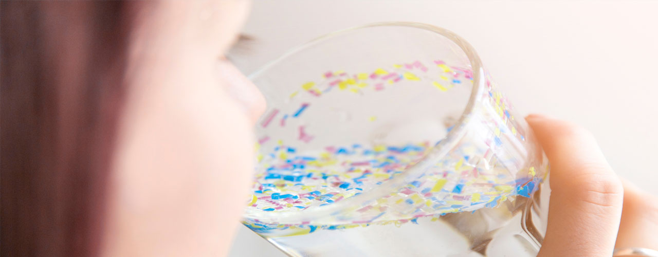 girl drinking glass of water with colored particles